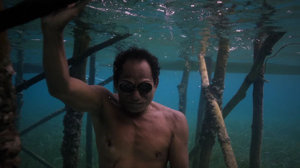 Plongeur bajau en apnée sous les pilotis d'un village sur l'eau avec lunettes en bois artisanales traditionnelles