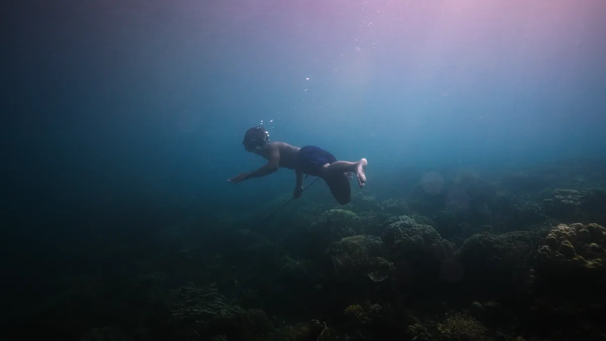 Plongeur bajau descendant en profondeur harpon à la main au-dessus d'un récif corallien en apnée