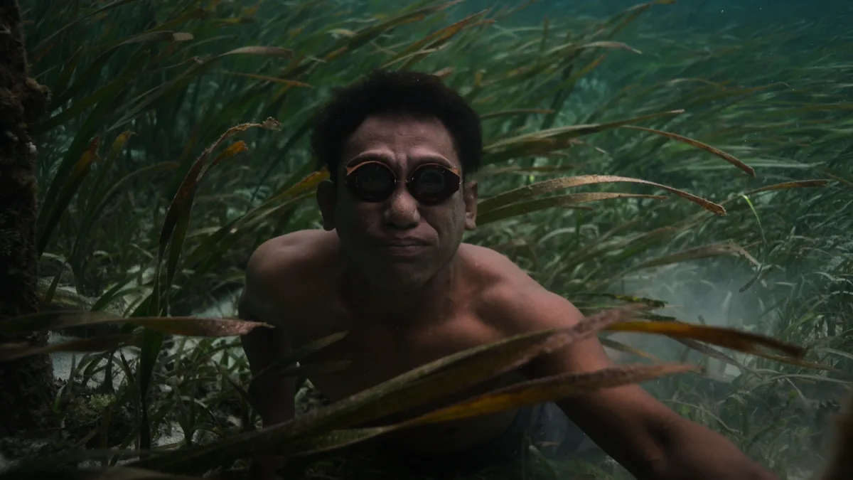 Silhouette d'un homme contemplant un village bajau sur pilotis au crépuscule sous un ciel d'orage en Indonésie