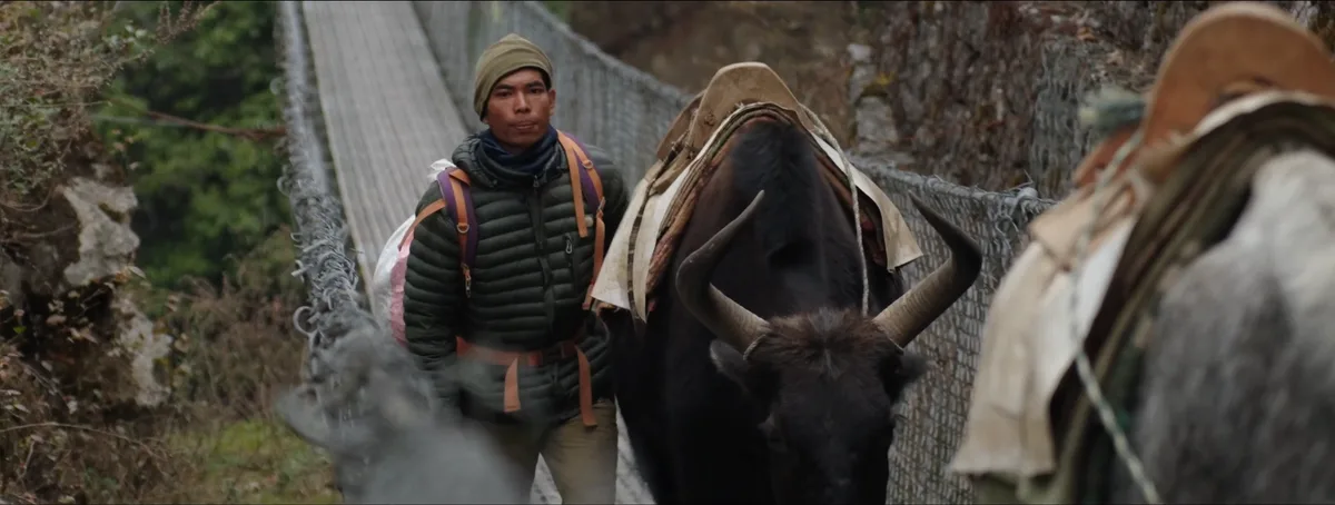 Porteur sherpa ajustant sa charge dans la vallée du Khumbu visage marqué par des années de travail en haute altitude