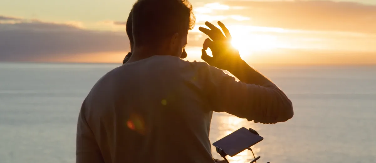 Vidéaste solo en silhouette pilotant un drone face au coucher de soleil sur l'océan tournage documentaire expédition